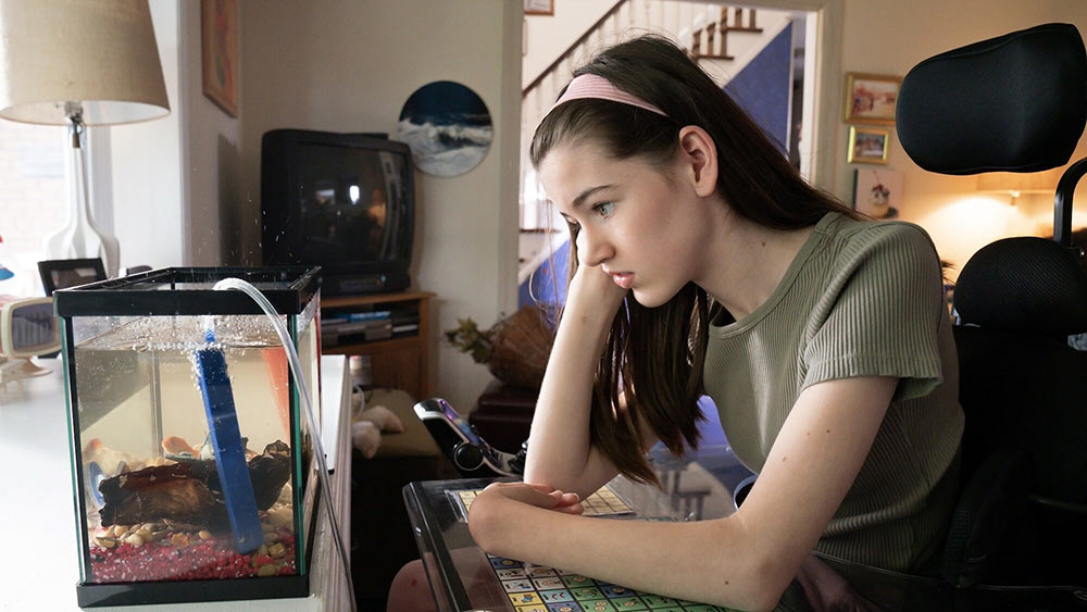girl in wheelchair leaning on a communications device staring into a fishtank