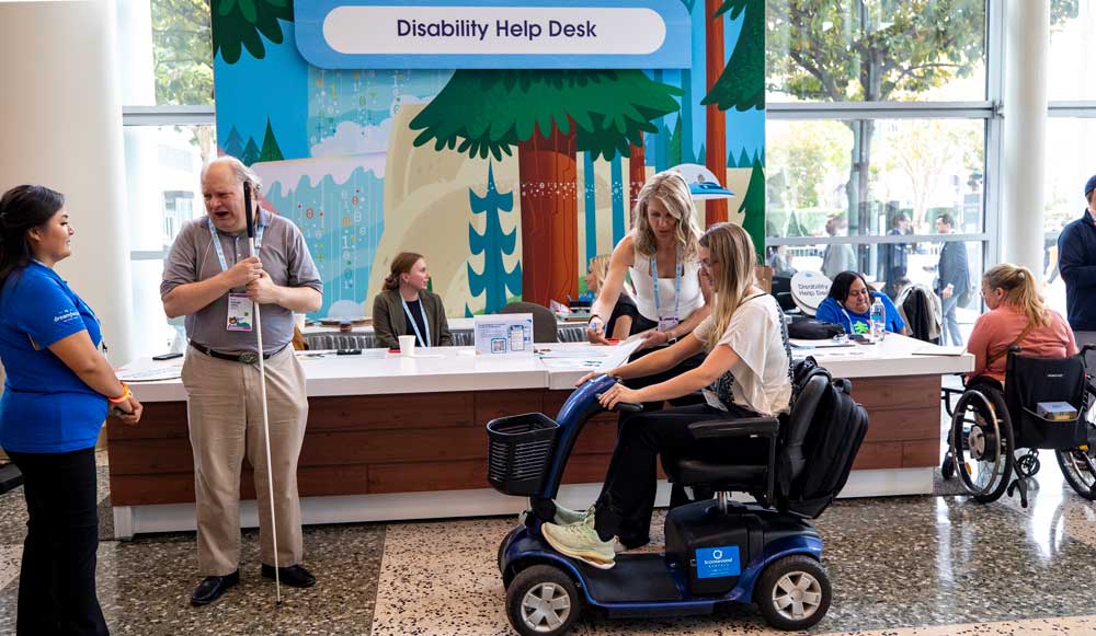 Woman working with another who is sitting on a mobility scooter in front of the accessibility help desk