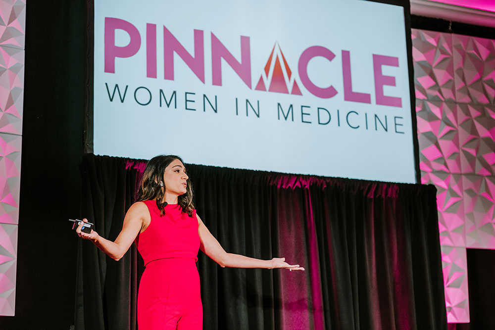 Woman on stage with screen that states Pinnacle women in medicine speaks while while gesturing to the audience