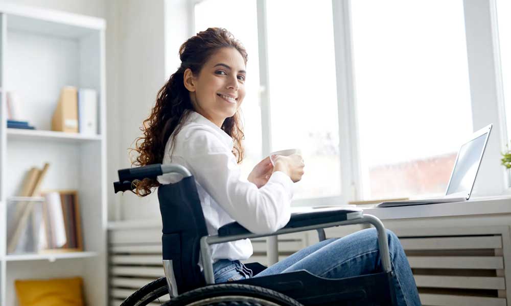 woman in wheel chair looks over her shoulder smiling toward the camera holding a cup of tea.