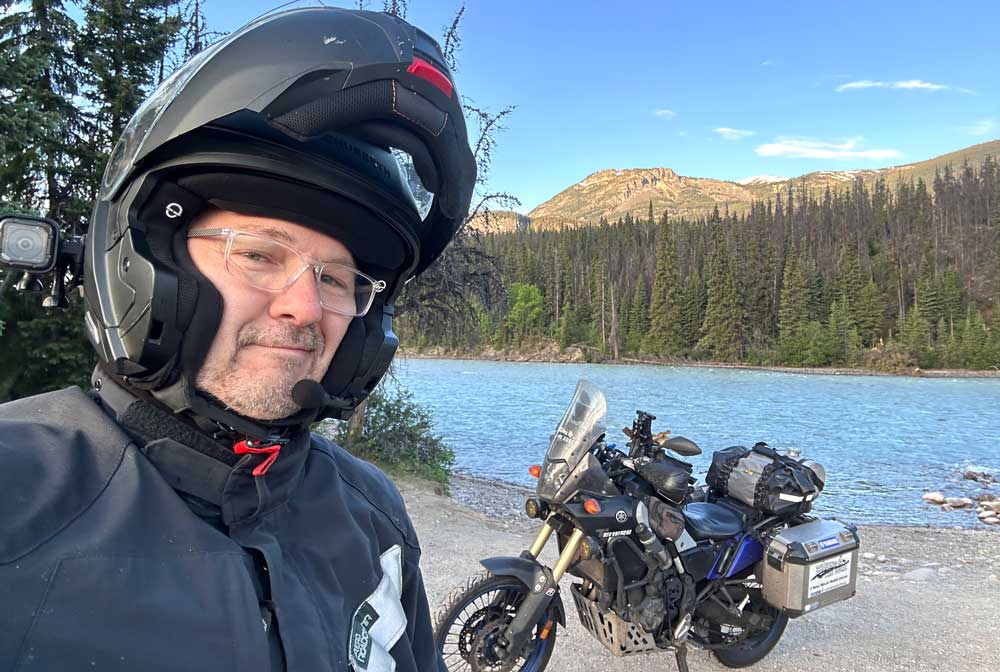 Paul takes a selfie of himself and his bike while standing in front of a mountain lake