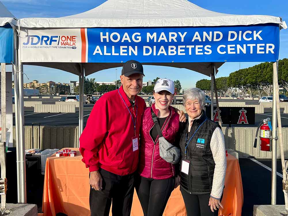young woman poses between an old man and woman below an outdoor event tent that says hoag mary and dick allen diabetes center