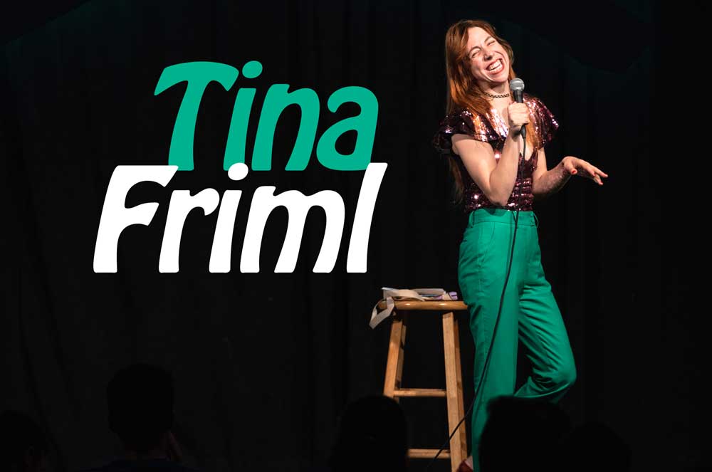 tina friml on stage doing stand up wearing green pants